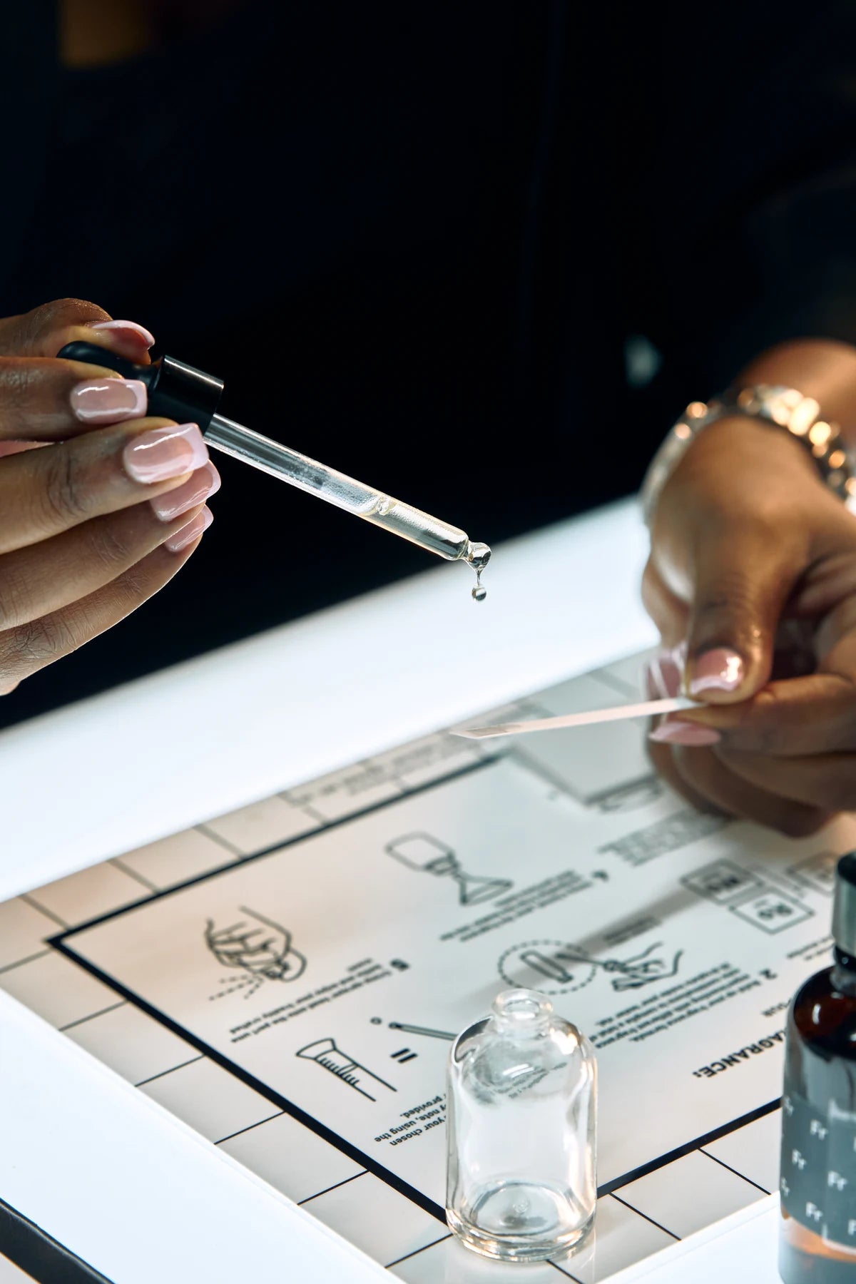 A drop suspended from a pipette above the Oo La Lab fragrance table